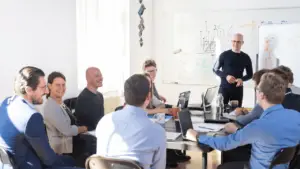 A group of professionals in a conference room discussing digital signage solutions, with a consultant leading the strategy session in front of a whiteboard.