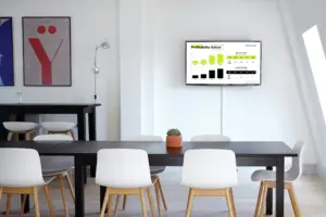 Wall-mounted digital signage screen displaying business dashboard analytics in a modern office meeting room, enhancing workplace communication and decision-making.